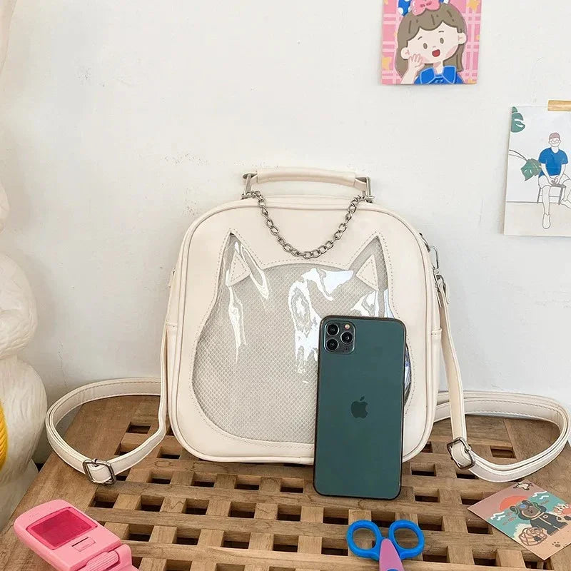 Cream cat ear ita bag flat lay next to a smartphone showing the feline silhouette and heart-shaped metal hardware.